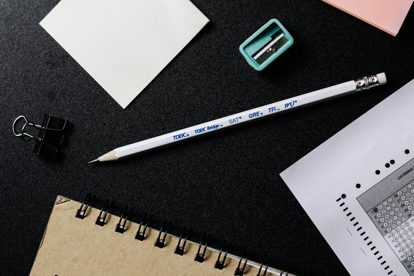 Materiales de preparación de exámenes y papelería dispuestos sobre una superficie oscura.